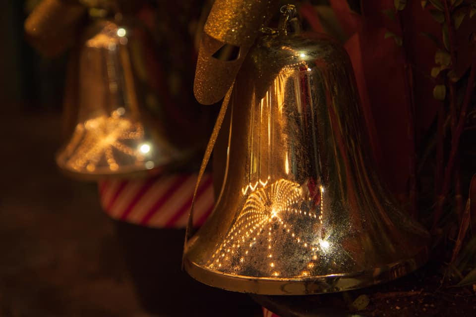 The twinkle of overhead Christmas lights is reflected in giant bells in the window boxes.